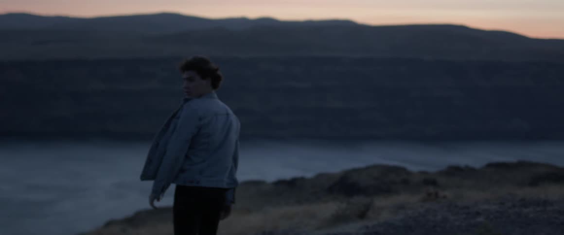 A man's jacket and hair blow in the wind at sunset