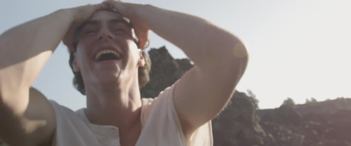 A man laughs and pushes his hair back