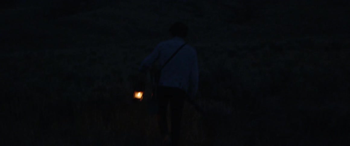 Person walks outside at night carrying a lantern