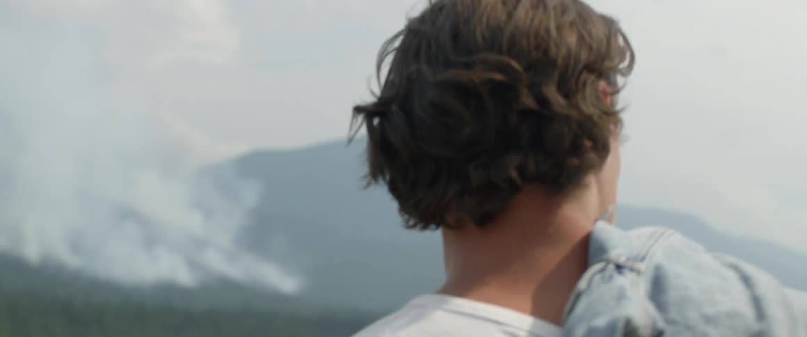 Man with a denim jacket stands in a field and looks around