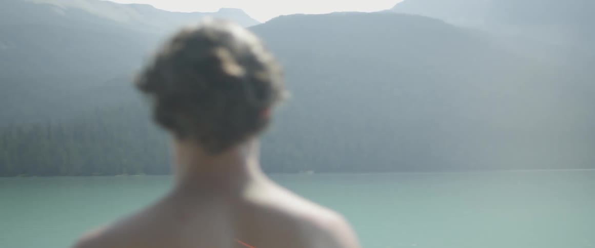 Man is standing and looking around in front of mountain lake