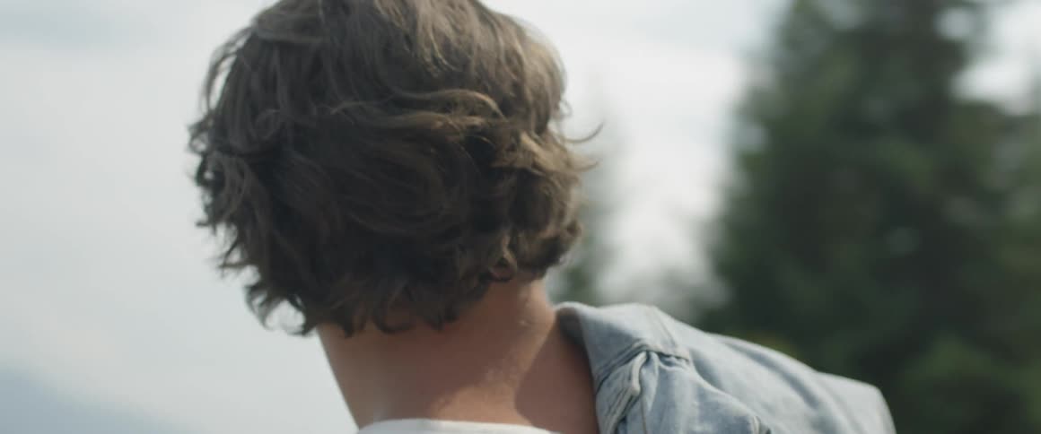 Man with a denim jacket stands in a field and looks around