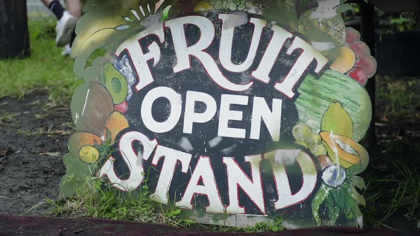 A painted fruit stand sign stands in the grass