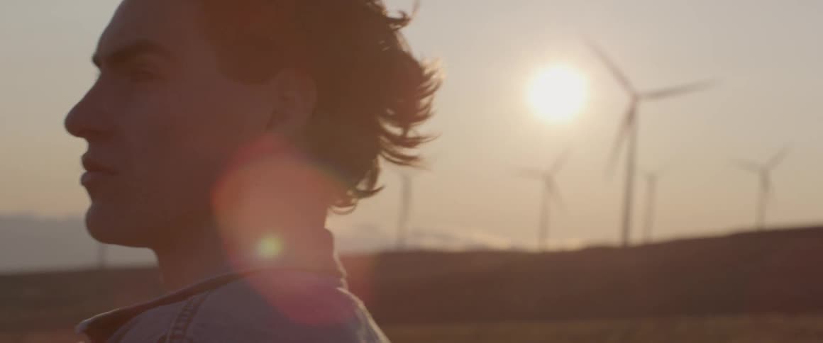 A man stands near a row of windmills
