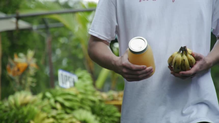 A man carries a jar and a bunch of bananas