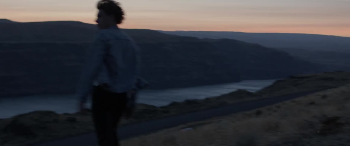 A man is walking in a natural setting at dusk towards a river basin
