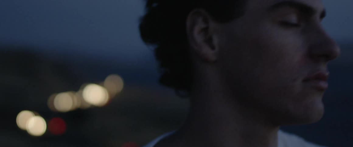 A man stands outside at dusk with his eyes closed as the wind blows his hair