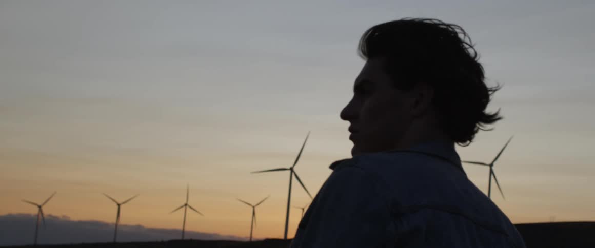 A man watches wind turbines spin at sunset