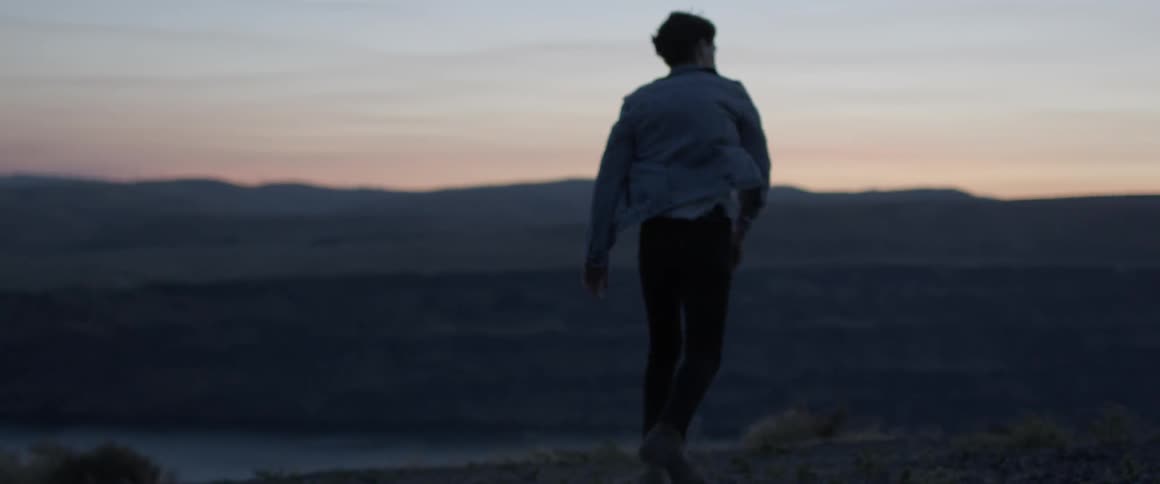 A man walks in a rural field at sunset