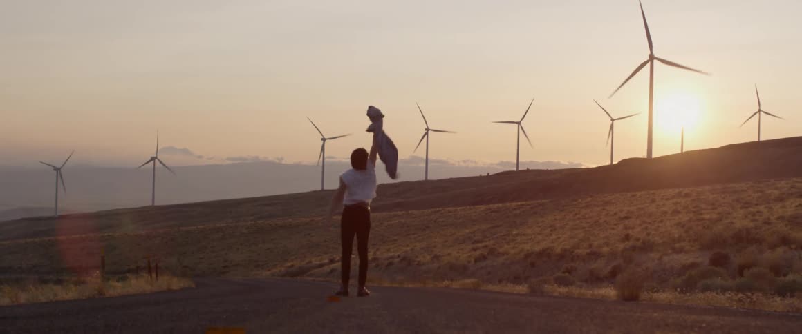 A man holds up and waves his jacket near wind turbines