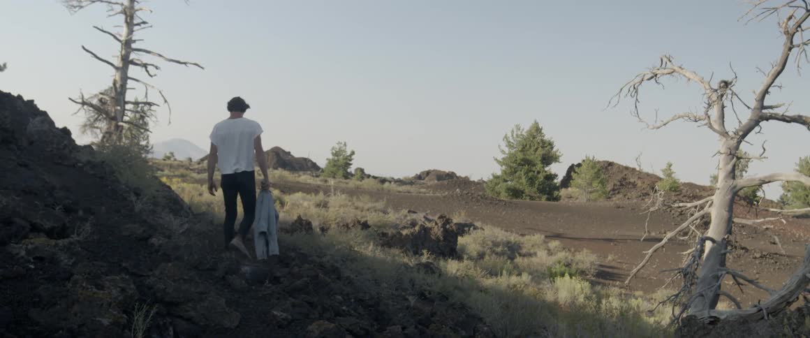 Man carries a denim jacket as he walks in a field