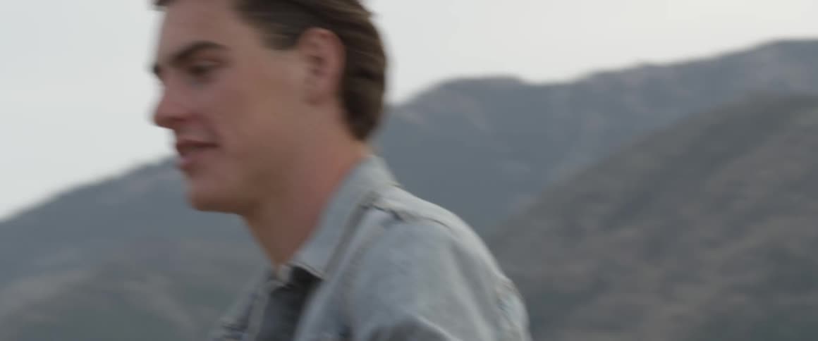 Smiling man hugs another person outside near mountains