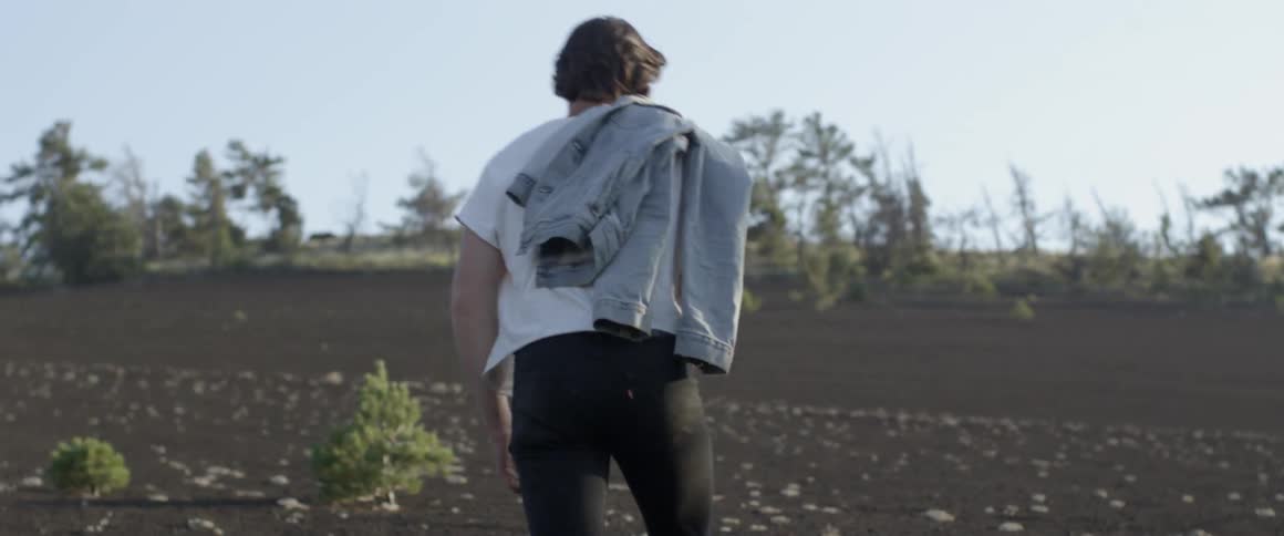 Man carries a denim jacket as he walks in a field