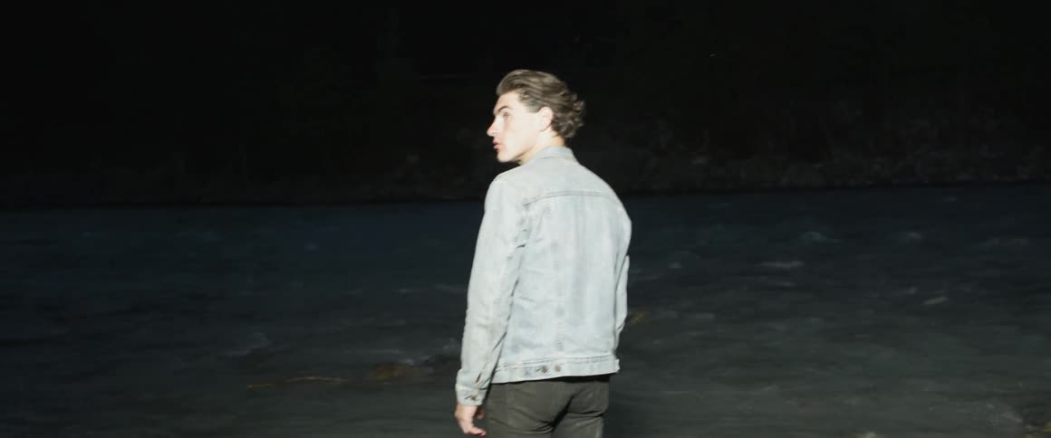A man standing by a river looks up and to the side
