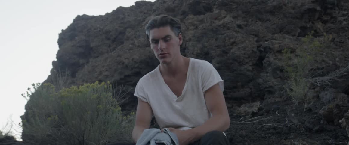 A man sits on the rocks holding his jacket