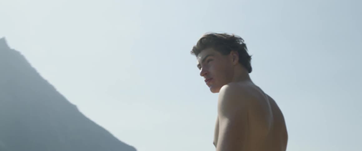 A shirtless man stands outside on a sunny day