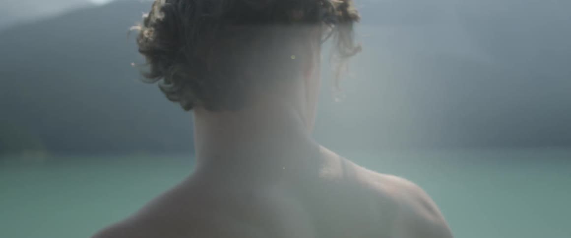 A man takes off his shirt and brushes his hair by the lake