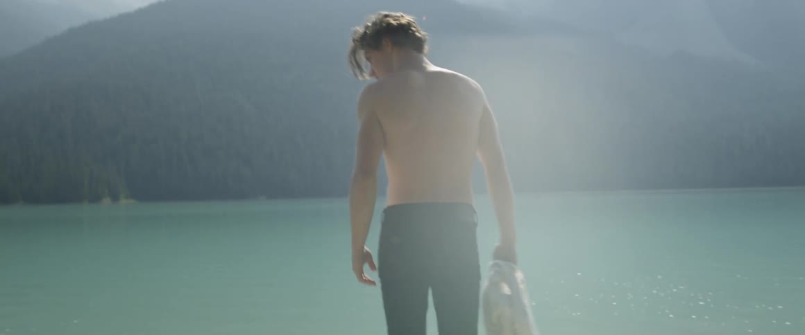 A man removes his shirt by the lake