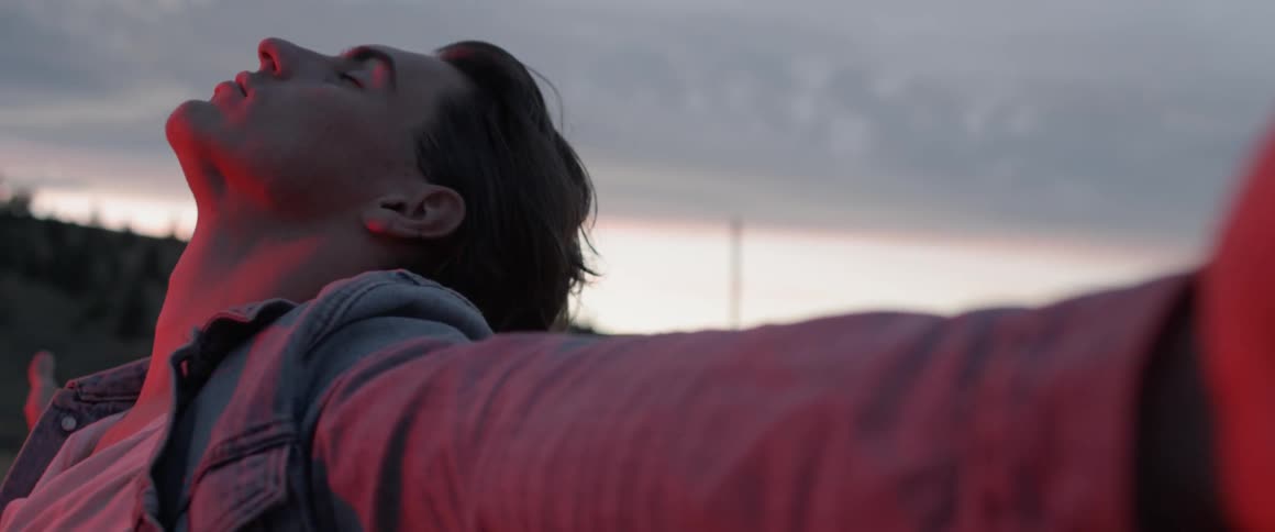 A man stretches out his arms and leans his head back at sunset