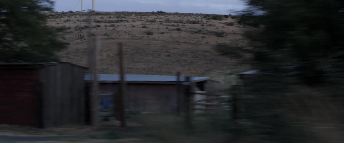 A car drives by a rural farm and wind turbine