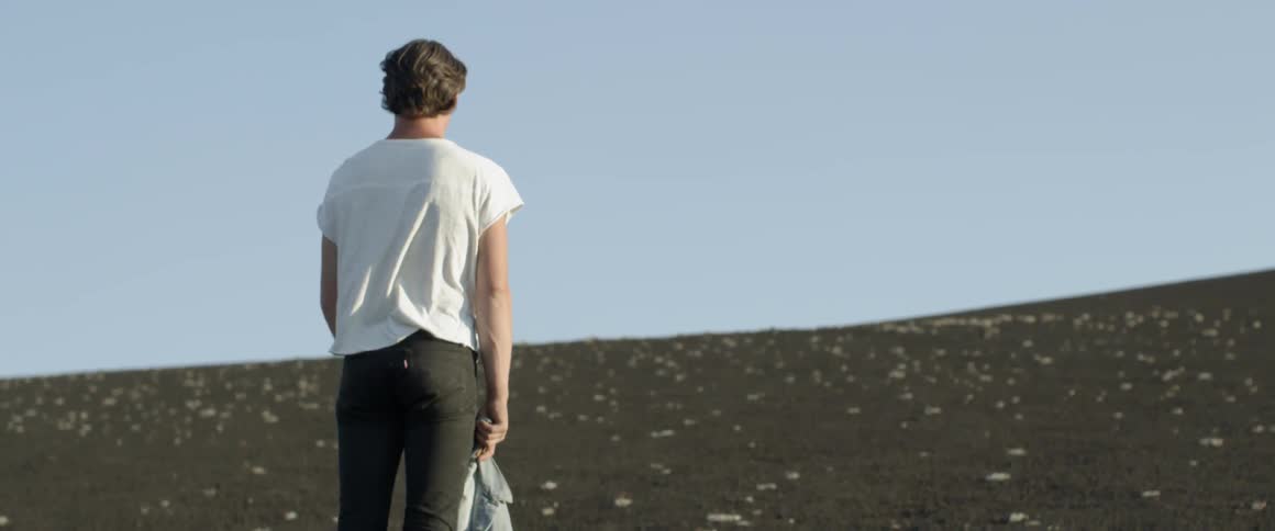 Man holds a denim jacket as he stands under a blue sky