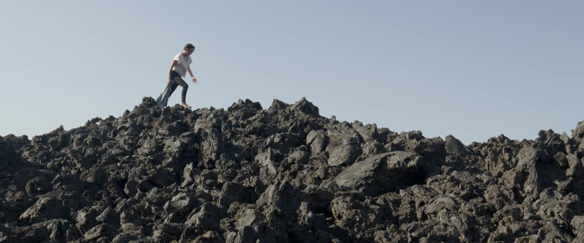 Man carries a denim jacket as he walks over the rocks