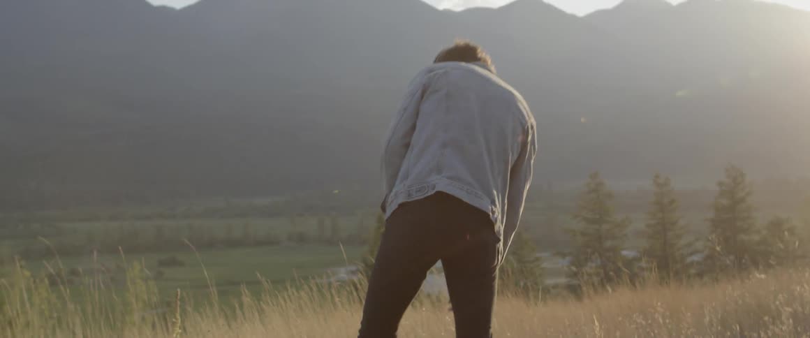 Man walks in nature and kneels down to pick a weed