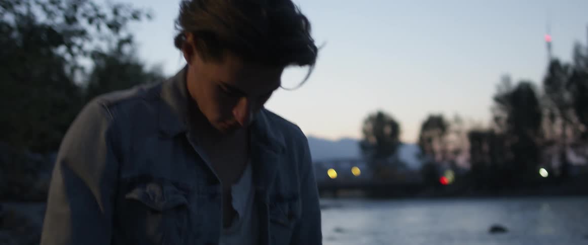 Man wearing a denim jacket stands near a pond