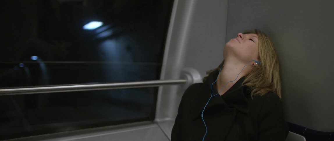 A woman sits on a subway rips earbuds from her ears