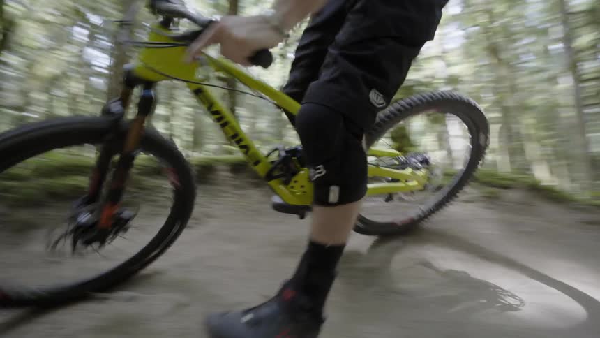 A man is filmed bicycling in a forest