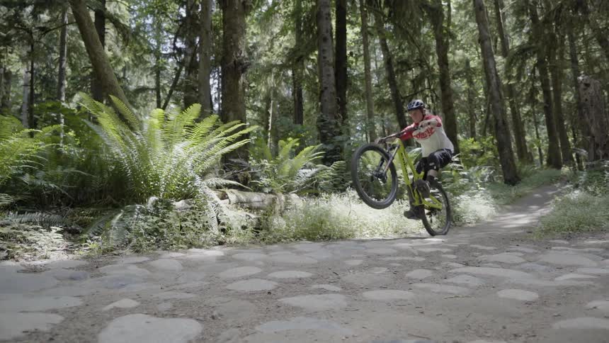 A person films a mountain biker popping a wheelie