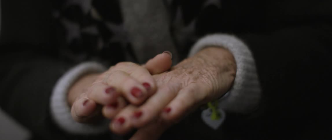 An elderly woman rubs her hands together