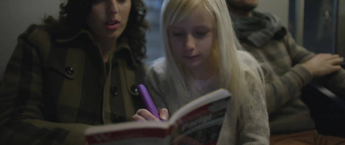 A woman and young girl read and outline a book while on a metro train