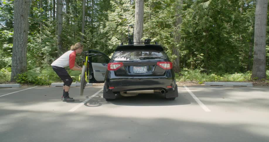 Man removes bike from rack on roof of car