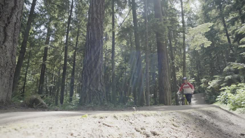 Man rides a bicycle in the forest as another man takes a photo of him
