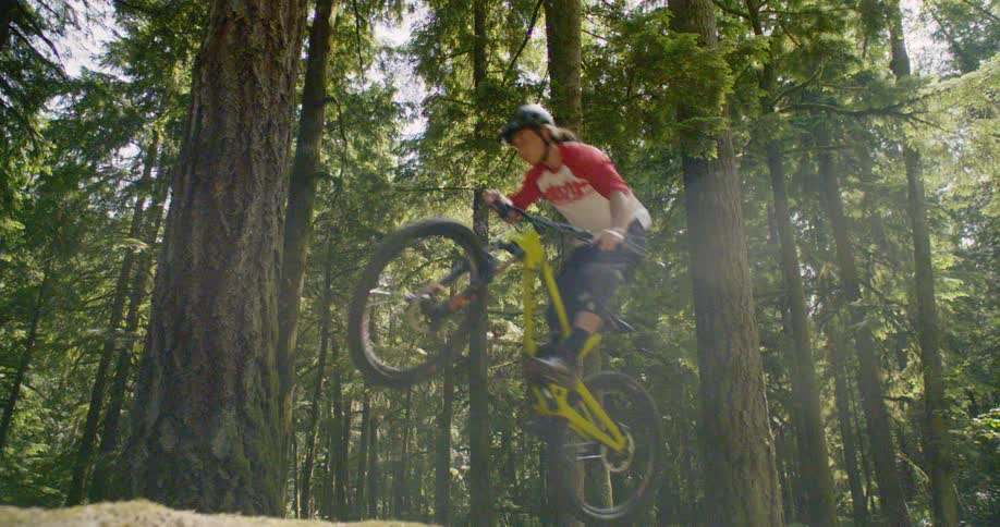 A person jumps on their bicycle in the forest