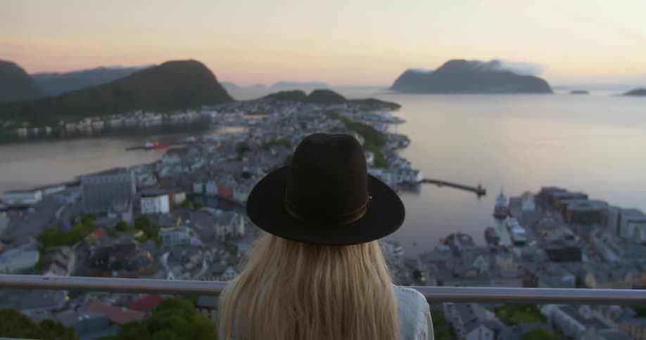 A woman overlooks an ocean town at sunset
