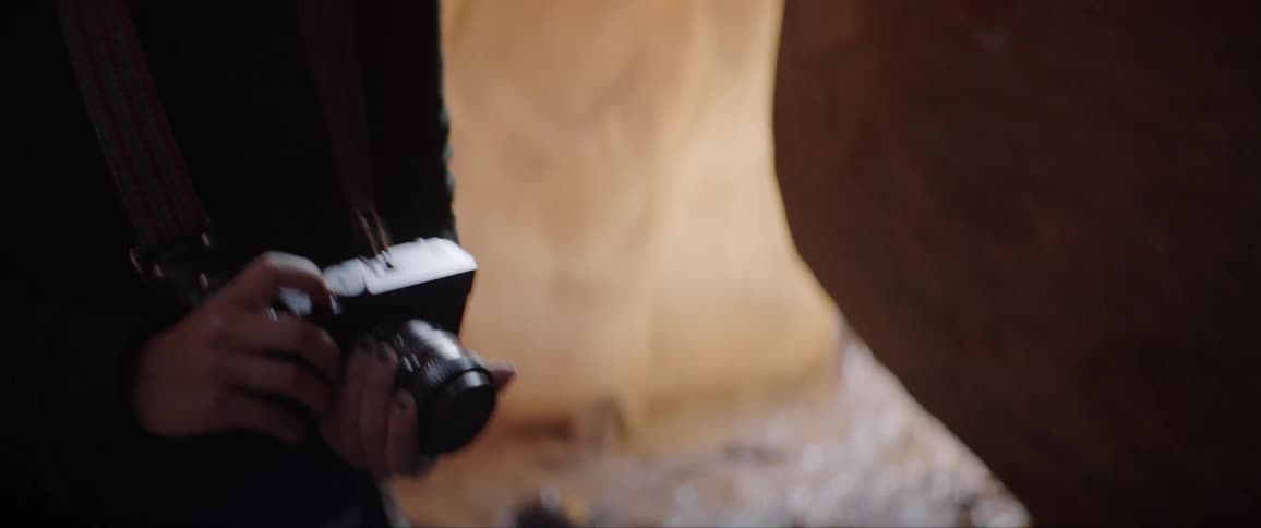 Woman standing in a cave holds a camera and looks up