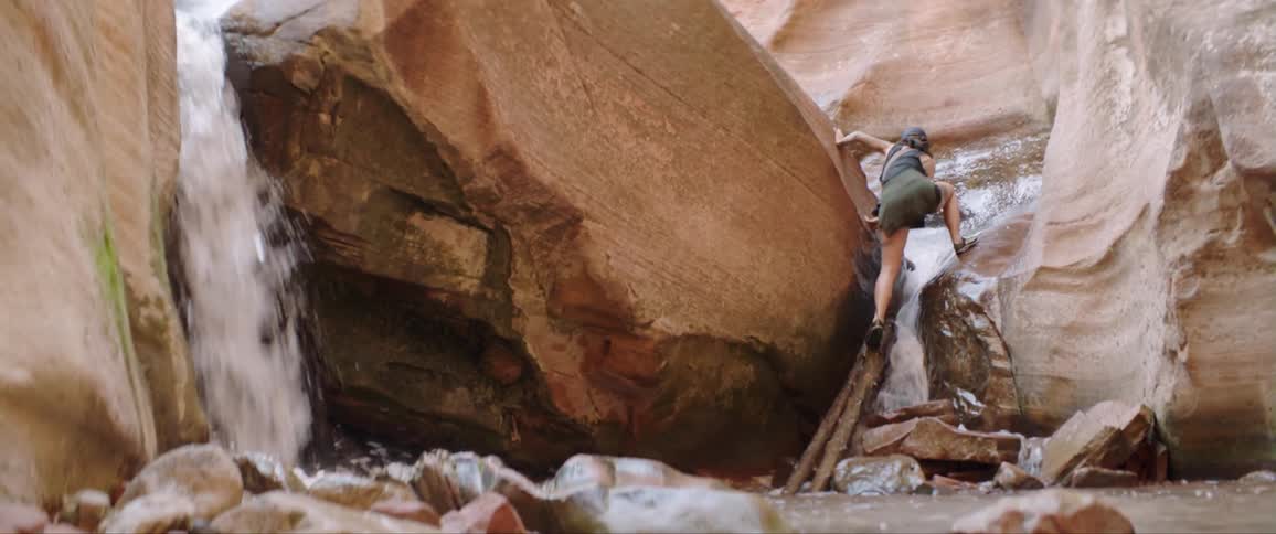 A woman climbs up on rocks and logs around flowing water