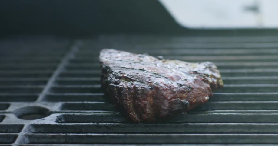Smoke rises around a steak cooking on a grill