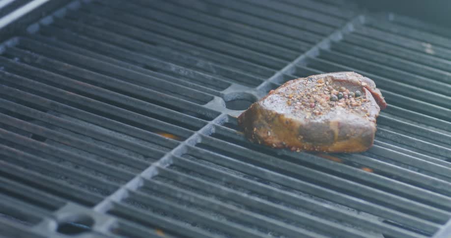 Thick steak is put on the grill over the flame