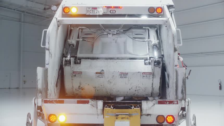 A garbage truck compacts with lights flashing