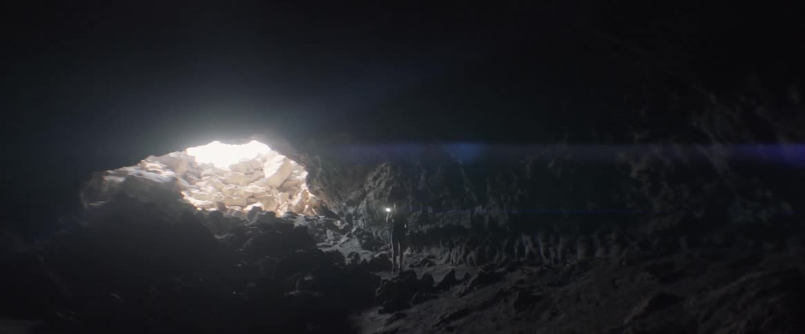 A woman carries a flashlight in a dark cave