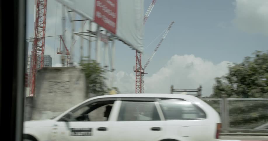 Cars travel on a highway past large cranes