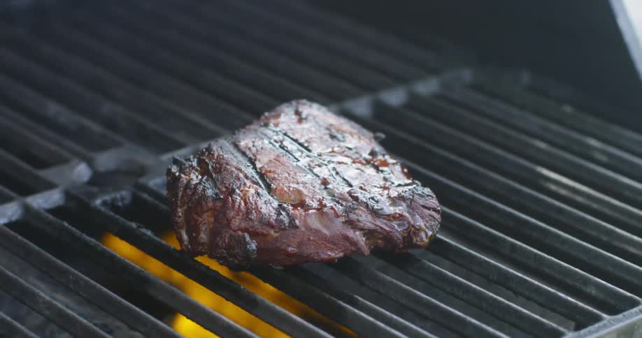 Steak sizzles on a grill with smoke surrounding it