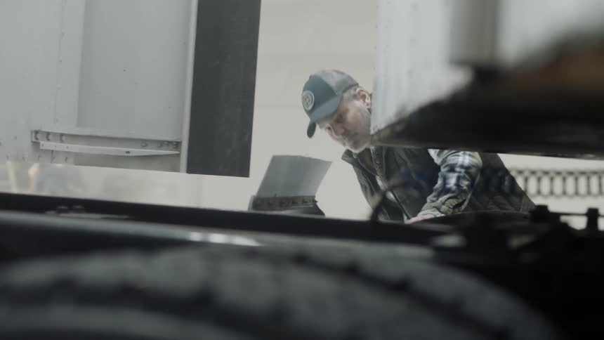 A man is inspecting a semi-truck inside a warehouse in daylight