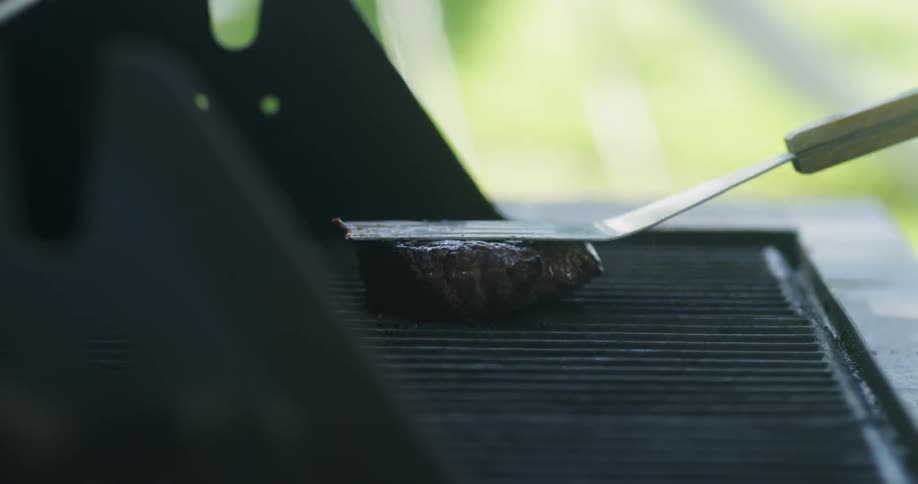 A person flips and presses down on a steak on the grill