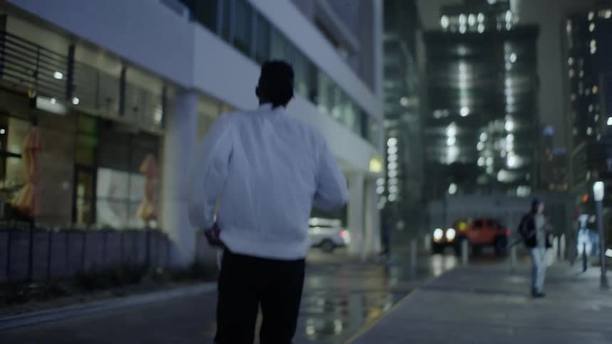 Man walks down a sidewalk in the city at night looking behind