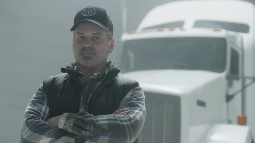 A trucker stands in front of a semi-truck