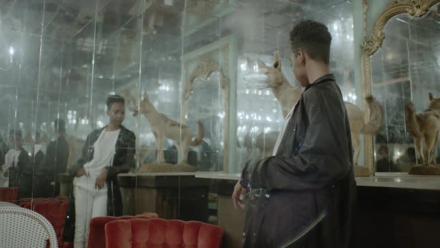 A man is approaching a woman standing indoors in front of a mirrored wall